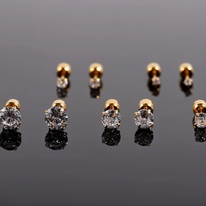 Macro shot of gold zircon stud earrings with screw backs displayed on black reflective surface