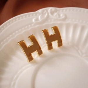 Close-up of H-shaped gold earrings with caramel enamel on a white ceramic tray