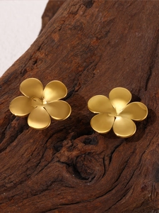 Macro shot of minimalist gold five-petal flower stud earrings on natural wood texture