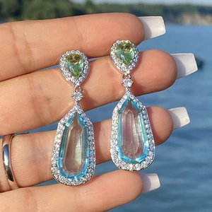 Close-up of double teardrop earrings with green and light blue zircon stones