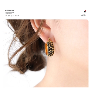 Close-up of a wide golden C-shaped earring with micro-set black stones on a model