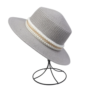 Close-up of grey straw sun hat with elegant pearl and gold chain band on a hat stand