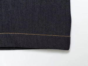 Détail de l'ourlet en denim bleu foncé avec surpiqûres jaunes et texture en sergé