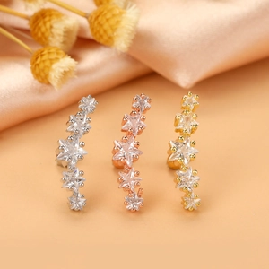 Close-up of star shaped cartilage earrings with zircon stones in silver, gold and rose gold