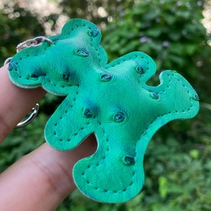 Close-up of green PU leather bear keychain with ostrich texture held in hand