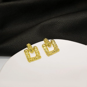 Macro view of gold-tone geometric rectangle earrings with lava texture on a sleek display