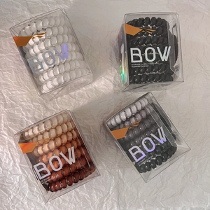 Set of four spiral hair ties in black, white, and gradient brown colors in boxes