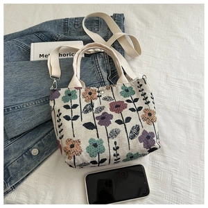 Detail of floral embroidery on beige canvas tote bag with adjustable shoulder strap