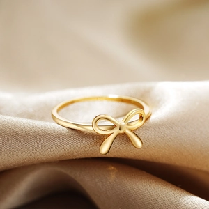 Elegant 18K gold bow-shaped ring displayed on luxurious gold silk fabric for women
