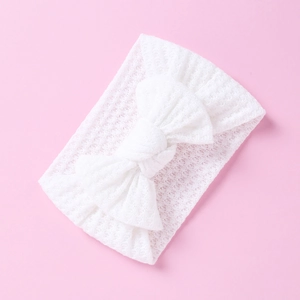 Macro shot of white knitted baby headband showing bow detail and hollow texture