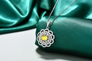 Détail macro d'un pendentif fleur argenté avec pierre jaune sur satin vert