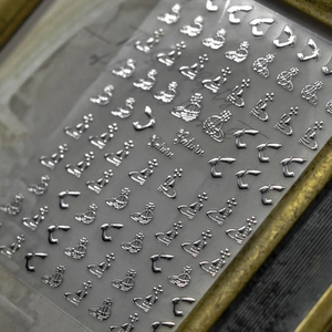 Macro detail of silver 3D embossed nail stickers featuring Saturn and orbital designs