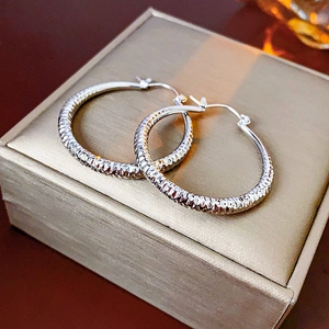 Détail de créoles argentées texturées présentées sur un écrin à bijoux doré de luxe
