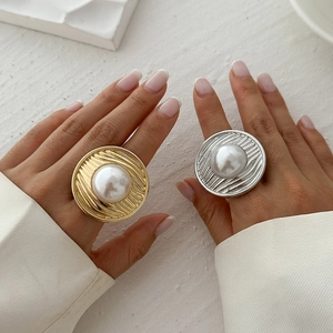 Detail of gold and silver textured metal rings with large faux pearls on a model hand