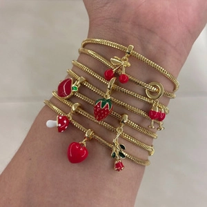 Detail of gold snake chain bracelet featuring red enamel strawberry and mushroom charms
