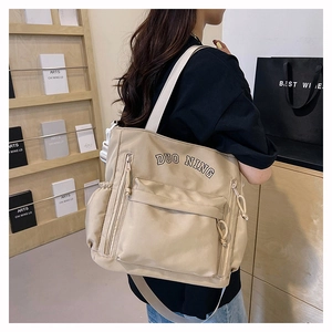 Detail of beige nylon tote bag with multi-pocket design shown on model in study room