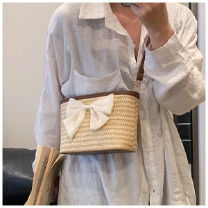 Close-up of woven straw bucket bag with dark brown leather trim and white silk bow