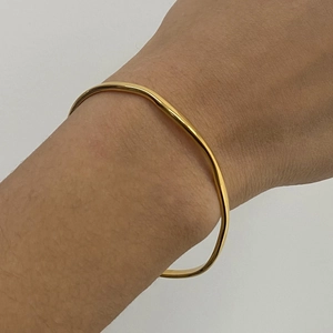 Close-up of a wavy gold stainless steel bracelet on a wrist with polished finish