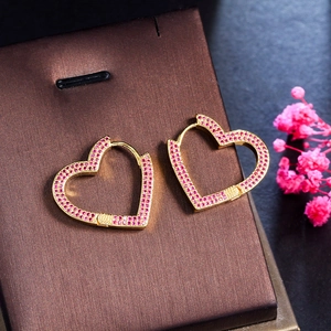 Dettaglio di orecchini a cuore dorati con zirconi rosa su una scatola da regalo
