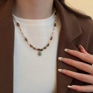 Detail of bohemian tiger eye beaded necklace with turquoise drop pendant on a model