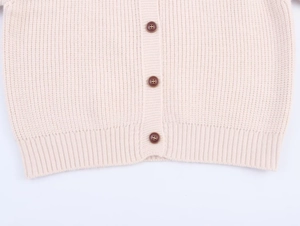 Detail of cream knit cardigan featuring ribbed hem and three dark brown round buttons