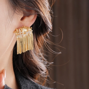 Gros plan de boucles d'oreilles à pompons dorés avec zircons portées par un modèle