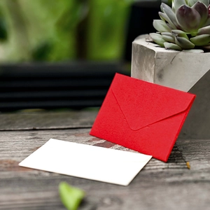 Mini red vintage triangular envelope and blank card on a wooden table with a succulent