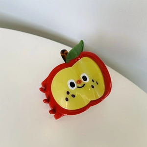 Detail view of red apple shark hair claw clip with smiling face and green leaf