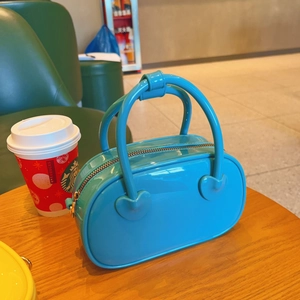 Detail of bright blue glossy jelly bag with heart-shaped hardware on a wooden table
