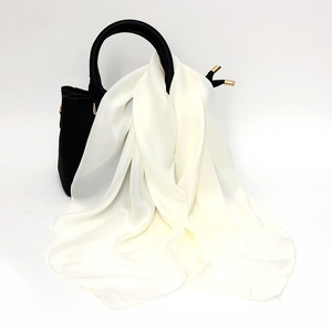 Close-up of a creamy white satin square scarf elegantly draped on a black leather handbag