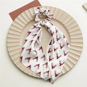 Dettaglio scrunchie in raso bianco con renne rosse e nastri lunghi su piatto decorativo