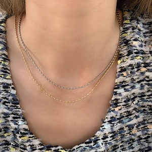 Detailed view of layered 18K gold and silver rice-bead necklaces on a female neck