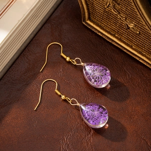Macro shot of purple dried flowers inside glass drop earrings on vintage leather