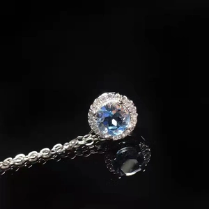 Macro shot of silver necklace with round blue gemstone and halo stones on black reflection