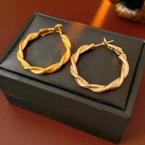 Macro shot of twisted gold hoop earrings with matte and polished interlaced textures