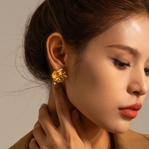 Golden rectangle textured earrings with wavy pleats shown on a model's ear