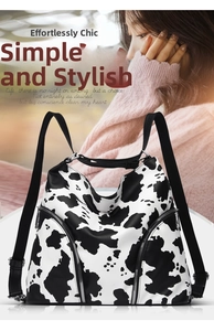 Detail of a cow print backpack featuring dual black straps and vertical side zipper pockets