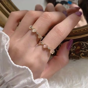 Detailed view of adjustable gold heart ring with pink cat eye stone on hand