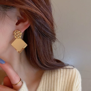 Detail of gold geometric square sequin earrings with circular woven texture on model