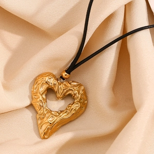 Close-up of hammered 18K gold-plated heart pendant on a black cord over silk fabric