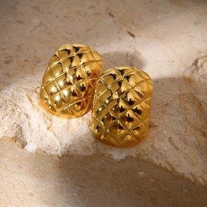 Detailed close-up of golden diamond-patterned stud earrings on a textured stone surface