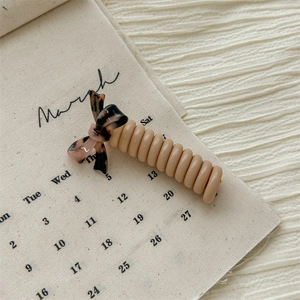 Close-up of beige spiral phone wire hair tie with a tortoiseshell bow detail