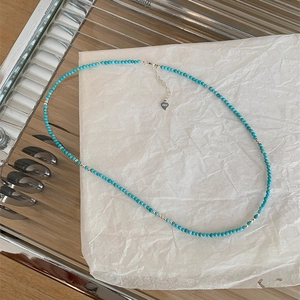Detail of turquoise beaded necklace with S925 silver clasp and heart charm on white paper