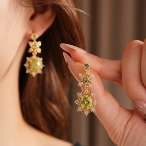 Gros plan de boucles d'oreilles vintage en or avec pierre verte ovale et zircons sur modèle
