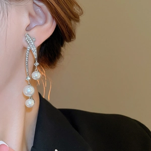 Détail de boucles d'oreilles longues argentées avec cristaux et perles portées par un mannequin