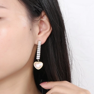 Detailed macro shot of long gold earrings with pink heart pendant and cubic zirconia