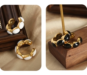 Detail view of retro gold-plated C-shaped ear cuffs with black and white enamel insets