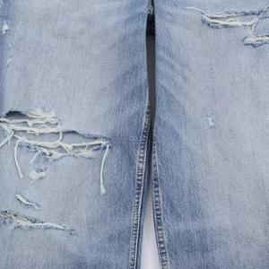 Détail du jean délavé avec déchirures montrant la texture du denim et les finitions
