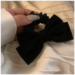 Detail showing hand holding a black velvet bow hair scrunchie with French style