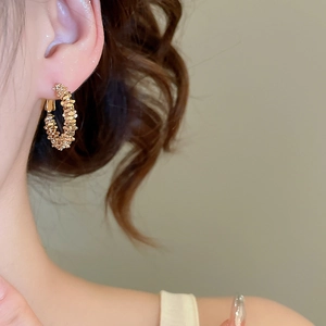 Detail of irregular textured gold hoop earrings on model showing premium metallic finish